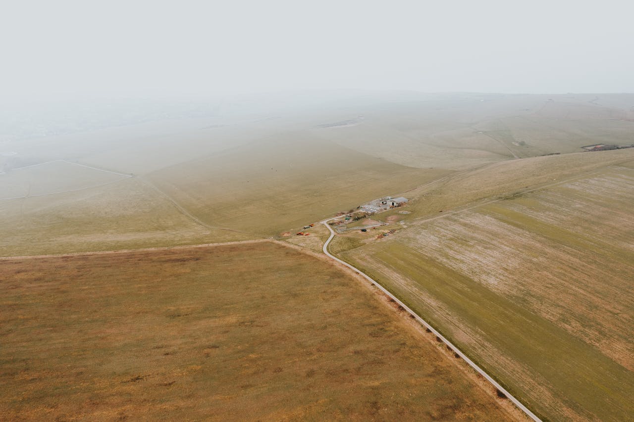 A serene aerial view of a foggy countryside landscape with a small road cutting through vast fields.